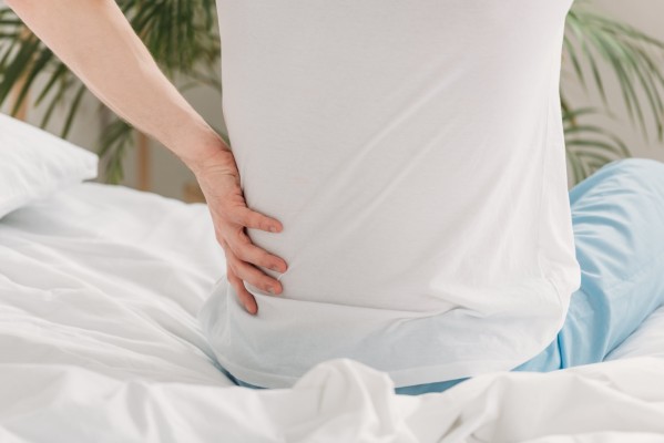 mężczyzna trzymający się za dolną część pleców podczas siedzenia na łóżku, ból kręgosłupa po wymianie materaca