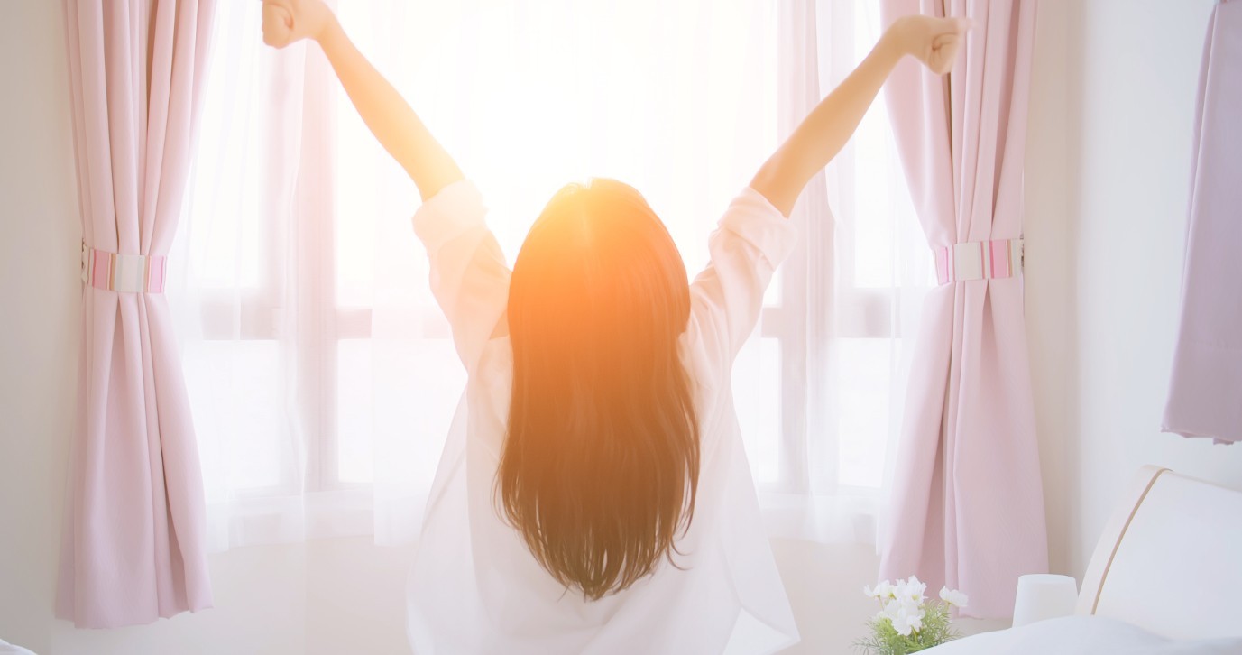 Kobieta o poranku wstająca z łóżka i rozciągająca ramiona w promieniach słońca po zdrowym śnie